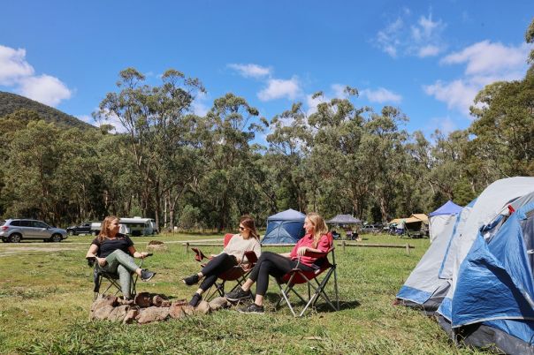 People sitting in front of tent in grassy clearing surrounded by forest