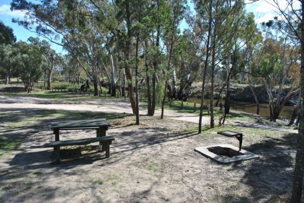 A campsite beside the river featuring a picnic table and campfire