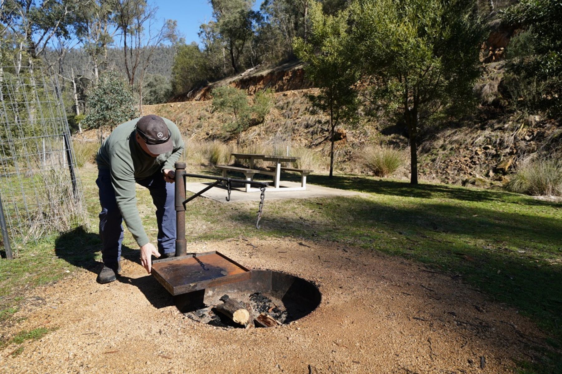 Man beside a campfire with a metal cooking plate
