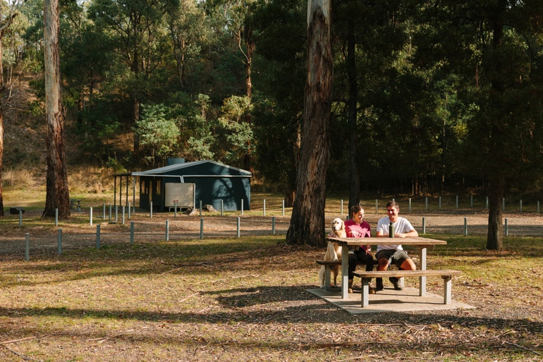 Two people at a picnic table with hut in background