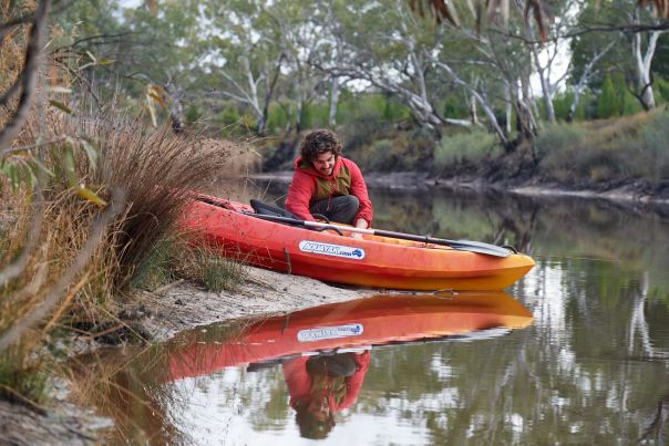 Two people push a red canoe into the water