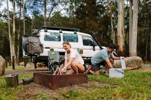 Two people setting up camp and a fire in front of a 4WD vehicle