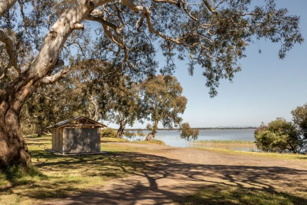 A toilet shelter overlooking a lake amongst a shaded tree area.