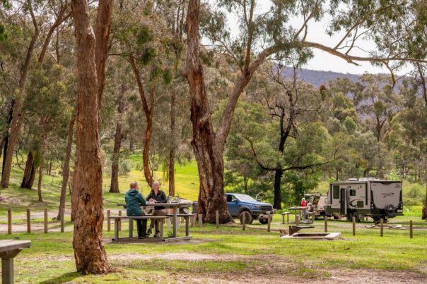 People sitting at a picnic table in a forest campground with a caravan in the background