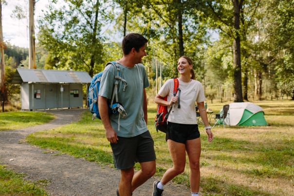 Two people walking in a clearing with a toilet building in the background