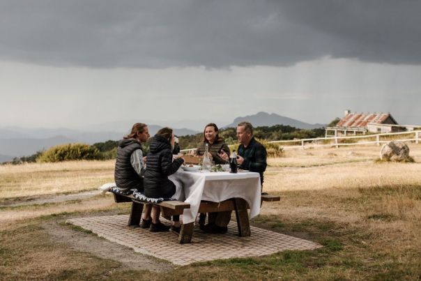People having a picnic at a table with a mountain hut in the background