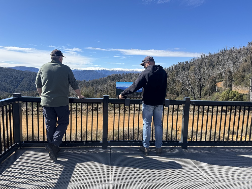 Two people  on a platform with mountains in the background