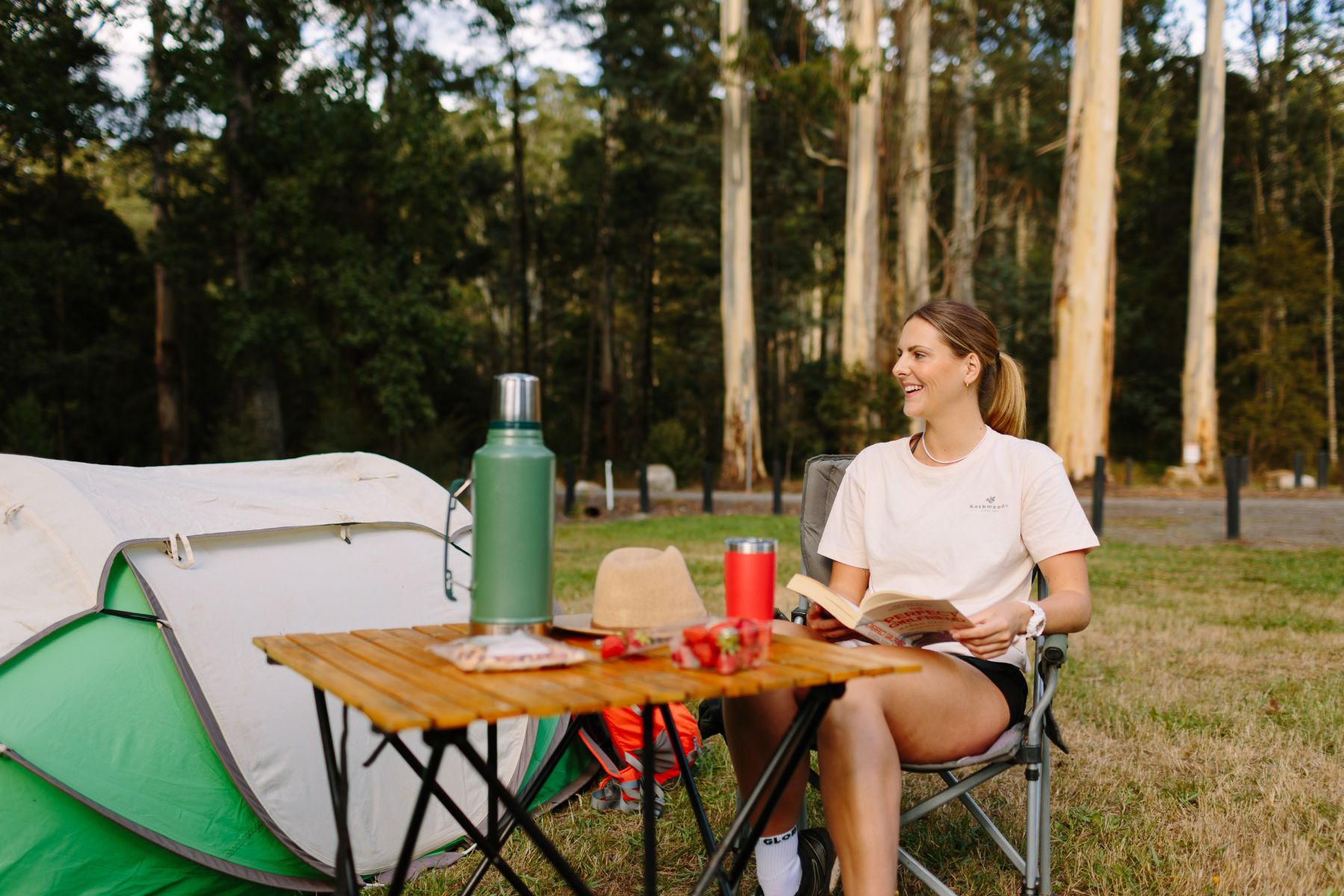 A person sitting reading in a book in front of a tent