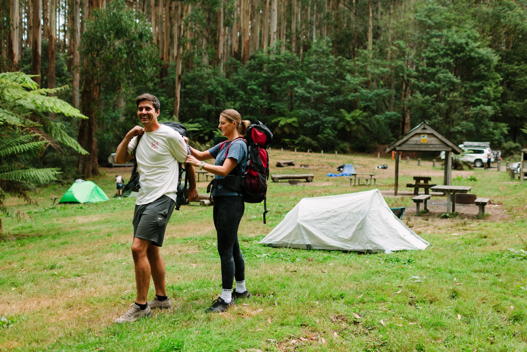 Two people with overnight backpacks in front of a tent in a grass clearing