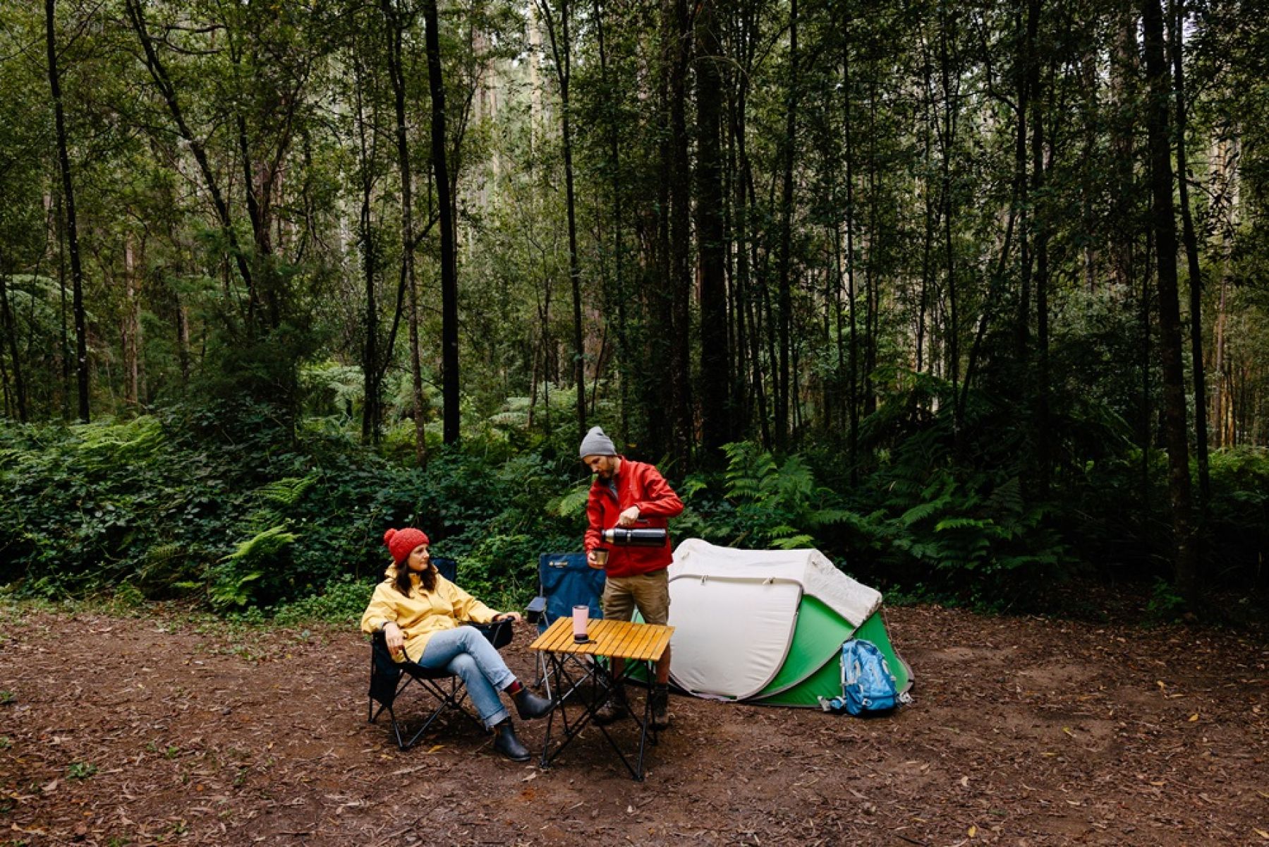 A tent and two people in a clearing surrounded by forest