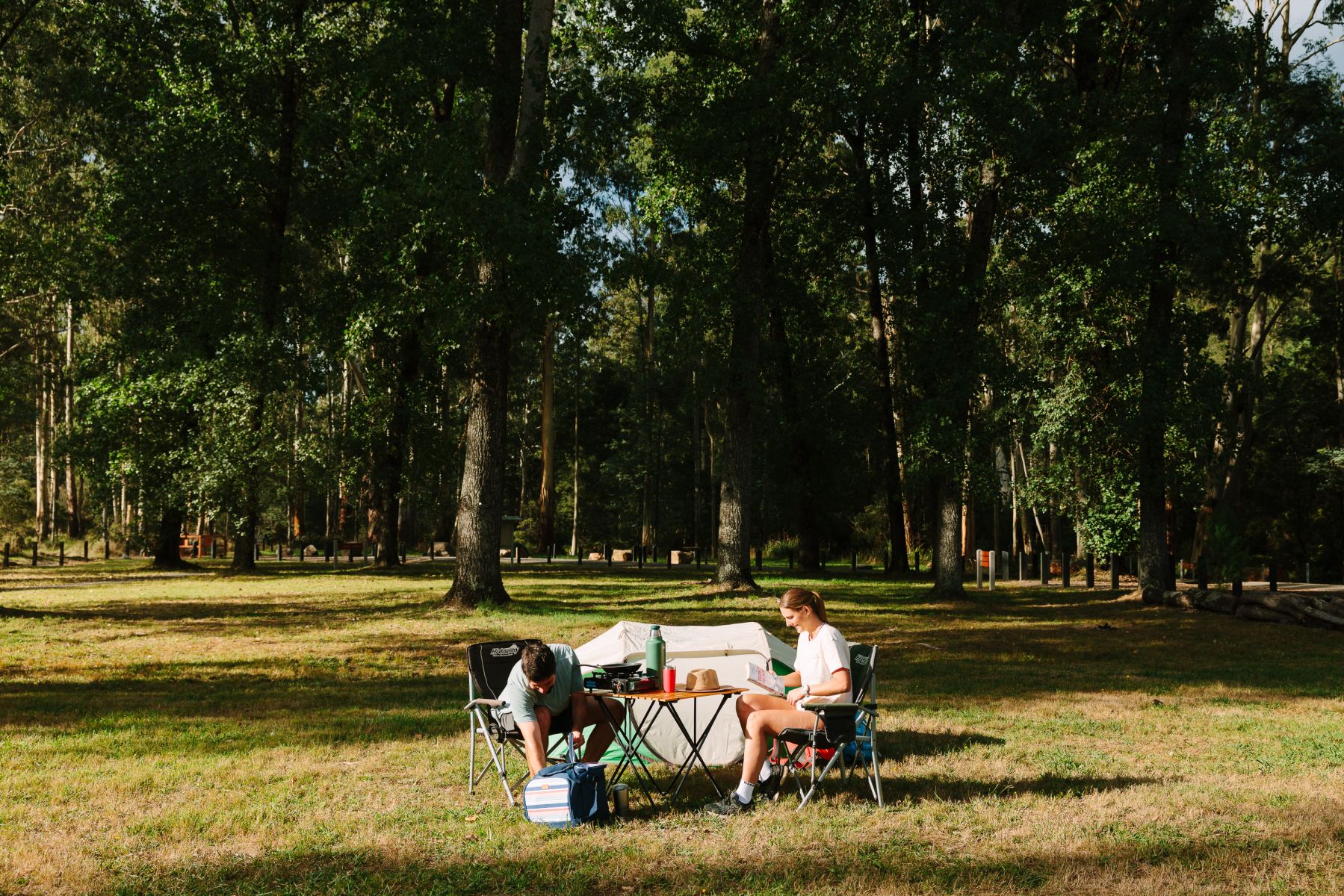 A person sitting in front of a tent in a large grass clearing