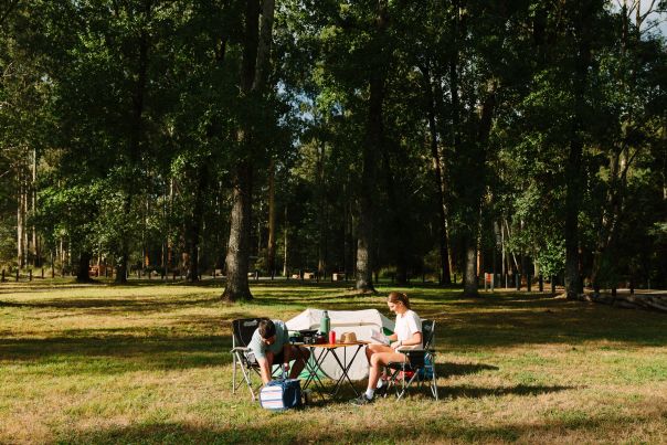A person sitting in front of a tent in a large grass clearing
