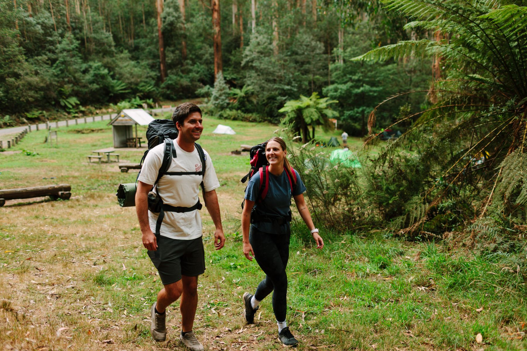 Two people with overnight backpacks walking through tall forest