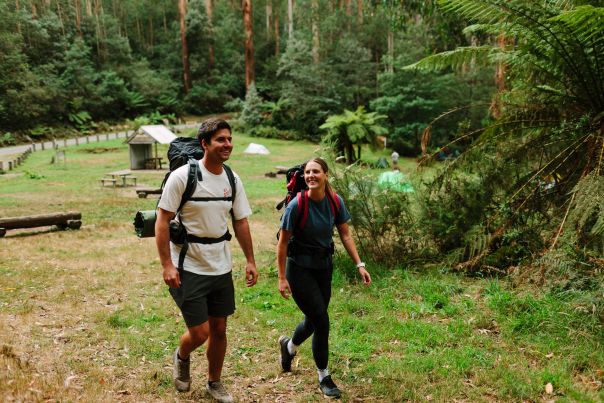 Two people with overnight backpacks walking through tall forest