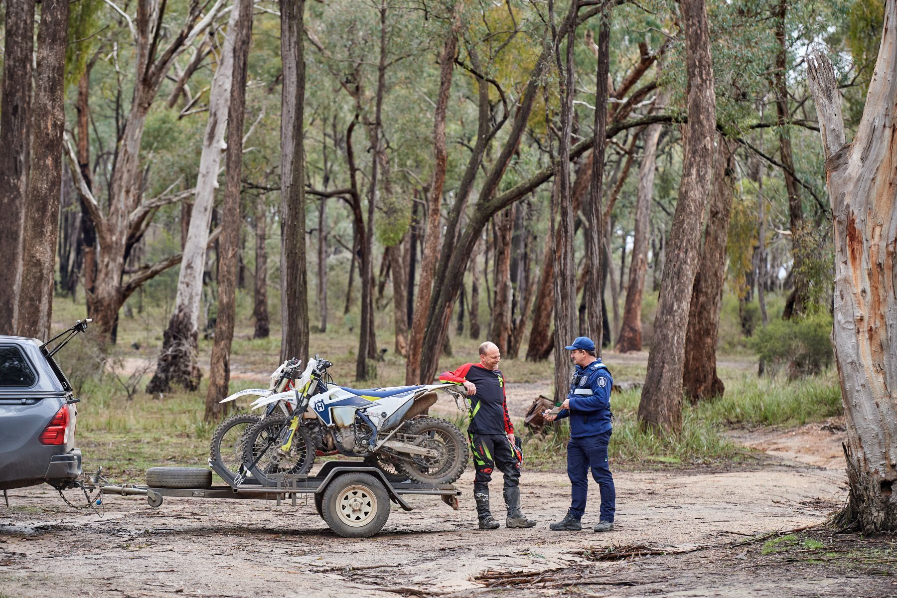 A trail rider with several bikes in a trailer speaks to an official in the bush