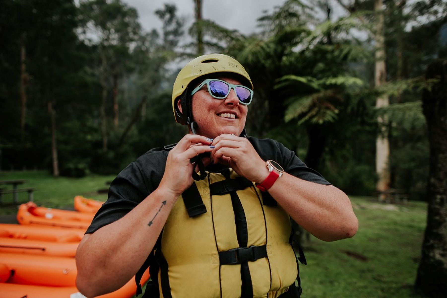 A person in a yellow life jacket putting on a helmet with canoes in the background.