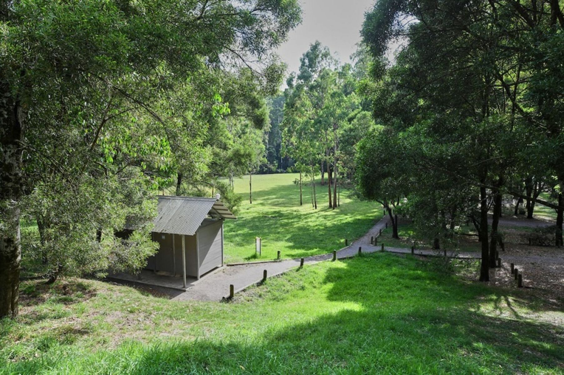 A grassy campground in the forest with a facilities block in the foreground