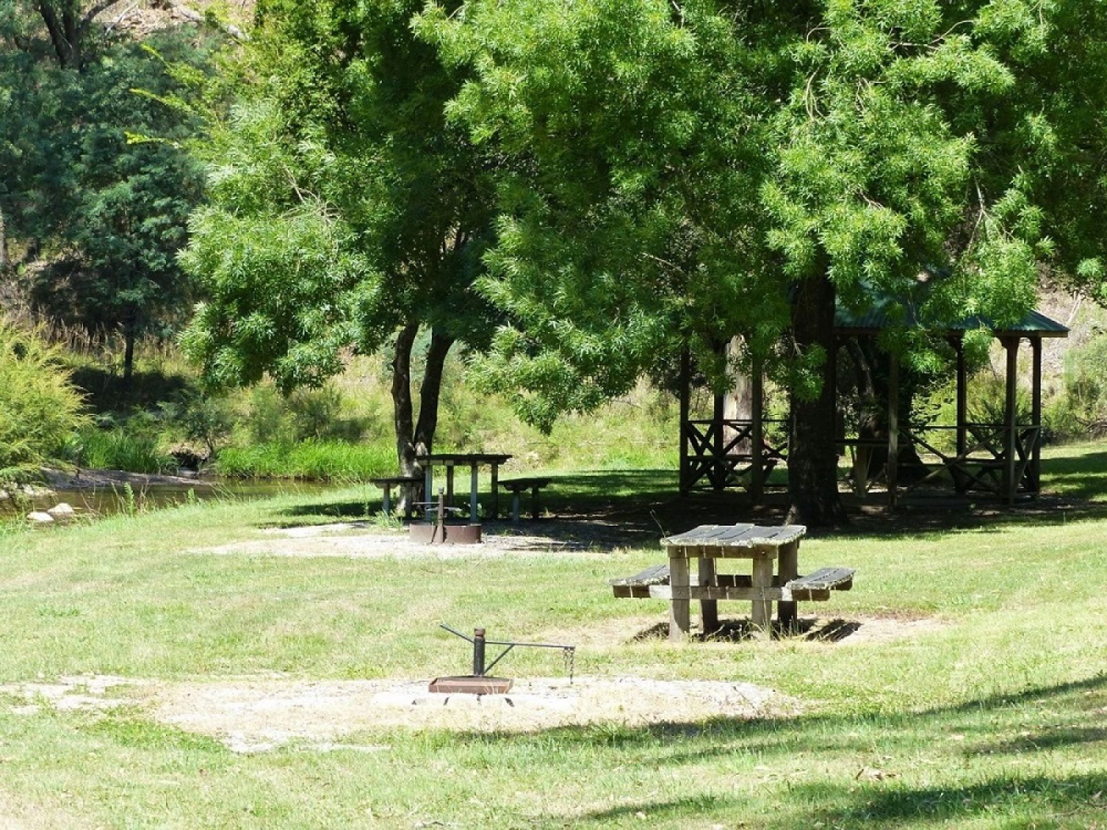 Picnic tables surrounded by a grassy area next to the Snowy Creek. 