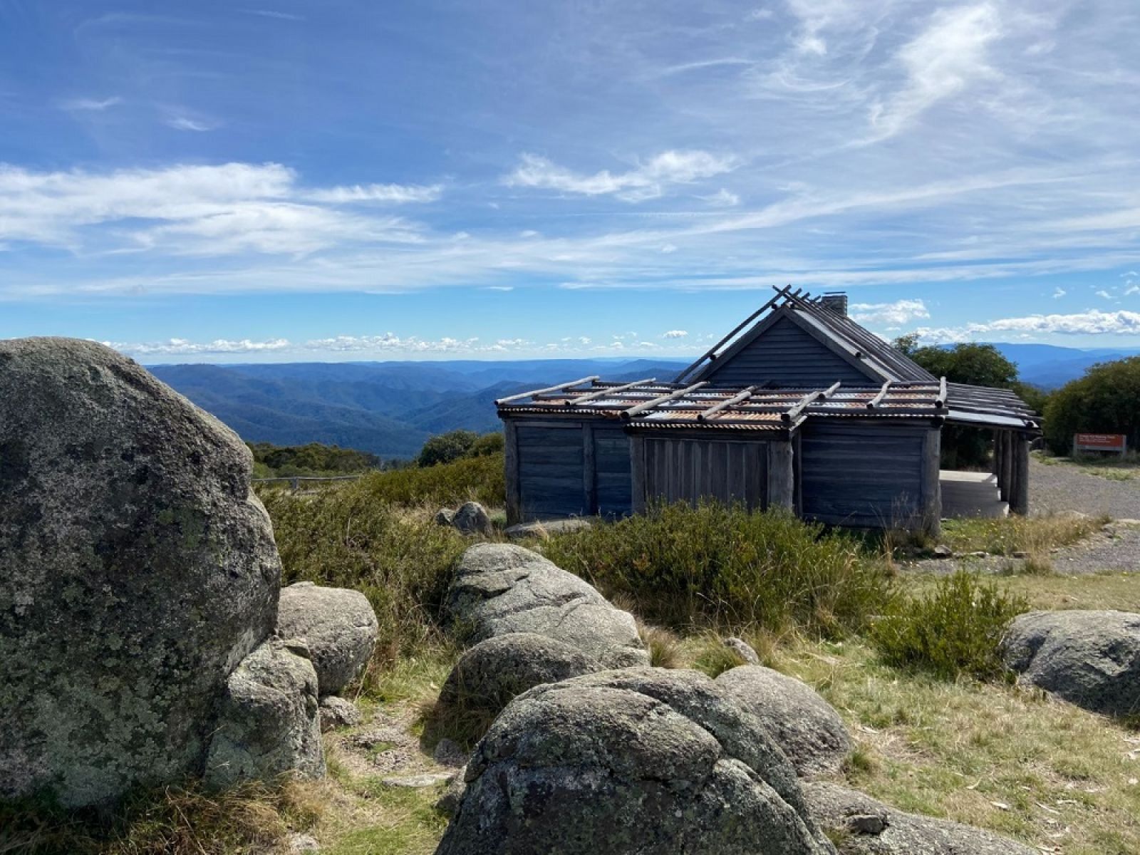 An old wooden hut surrounded large bounlders with an expansive forest view beyond.