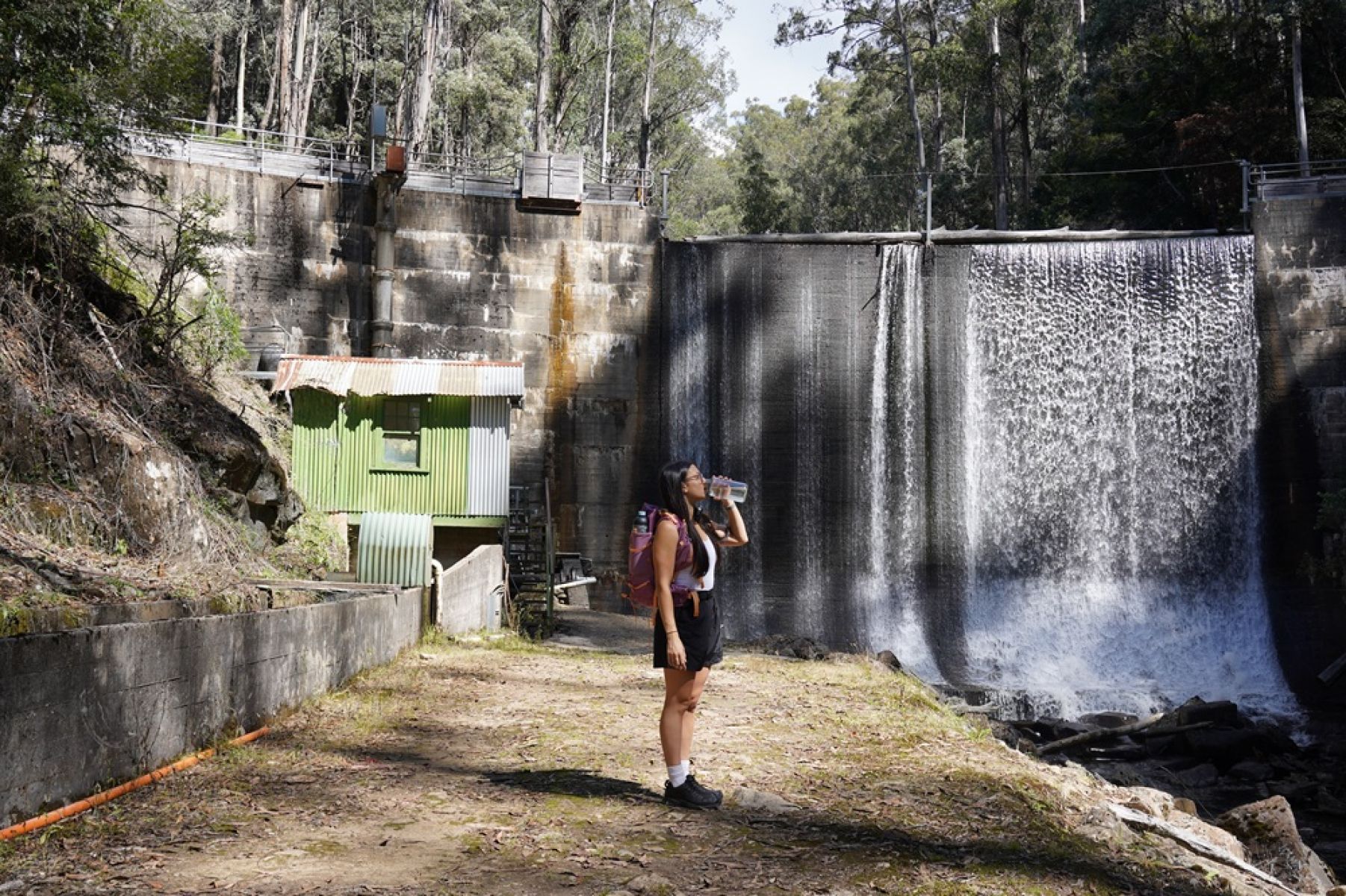 A person standing beside the dam wall drinking a bottle of water. 
