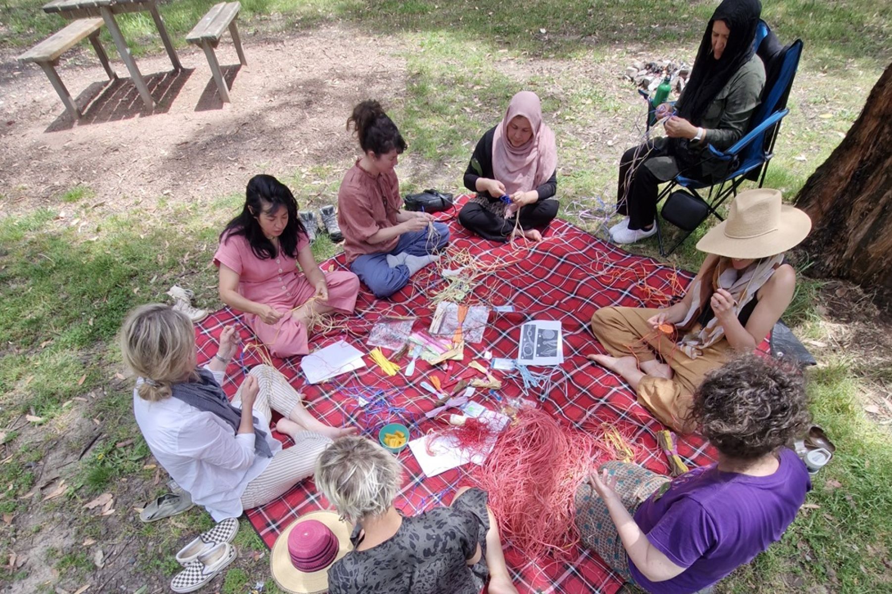 A group of people sitting basket weaving, surrounded by forest