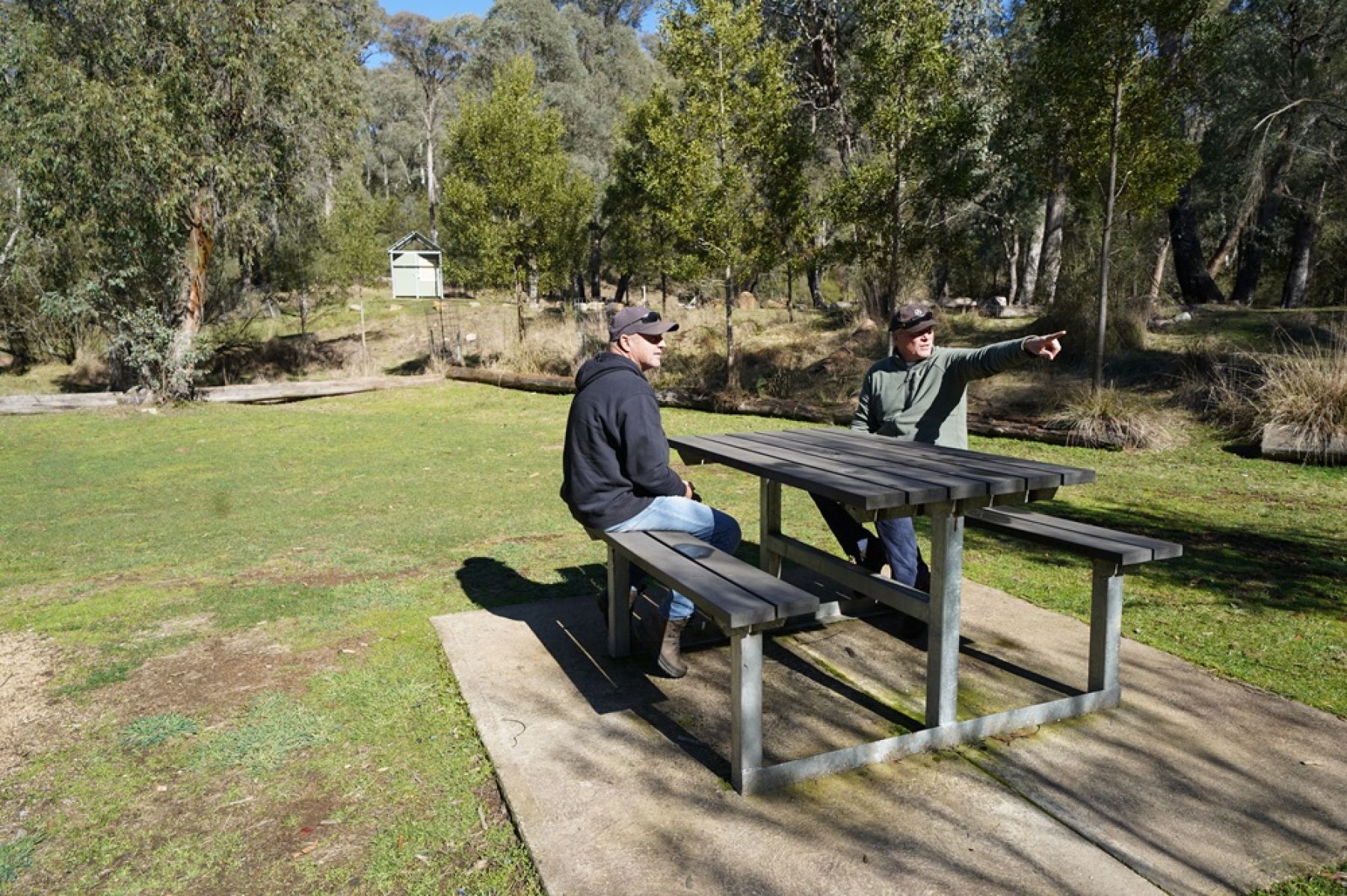 Two people sitting at a picnic table in a grassy clearing