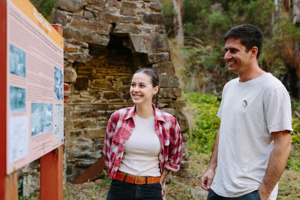 Two people looking at a sign with an old chimney in background