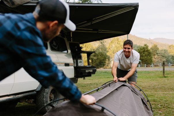 Two people setting up a swag in a grass campground