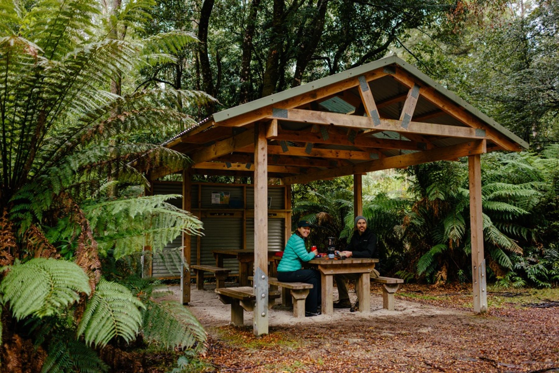 Two people sitting at a picnic shelter in the forest. 