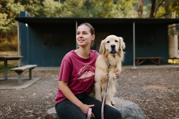 A person and golden retriever dog in front of a hut