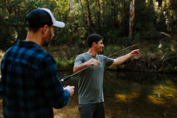Two people with a fishing line beside a river