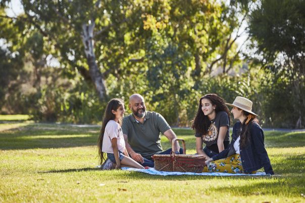 Four people sitting on a picnic rug with a picnic basket.