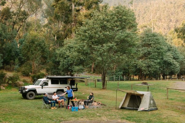 Group of people beside a tent and 4WD vehicle in an open grass campground