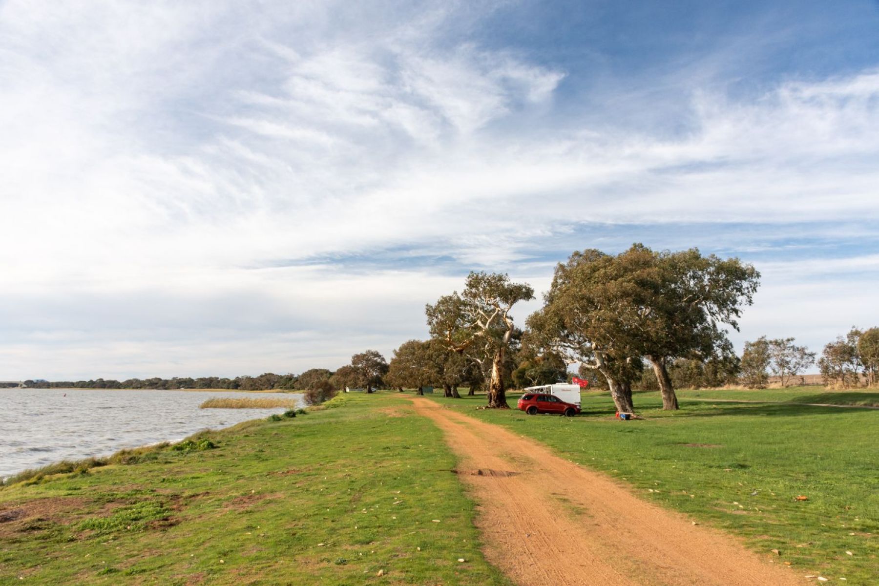 A car and caravan parked long a grassy shoreline.